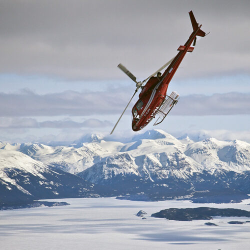 Red A Star helicopter flies at extreme angle with snow capped peaks in the background