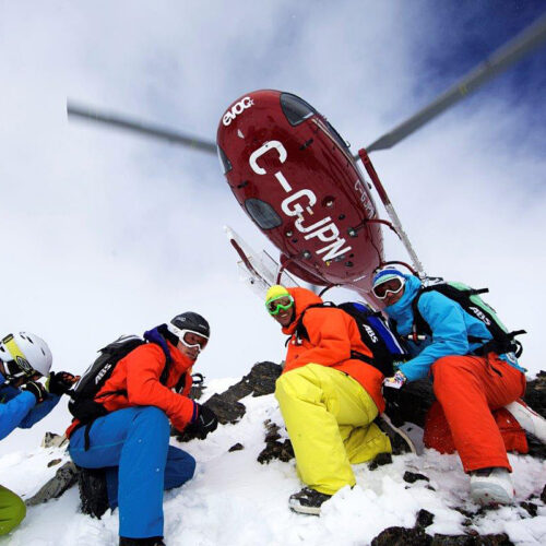Skiers crouch below helicopter