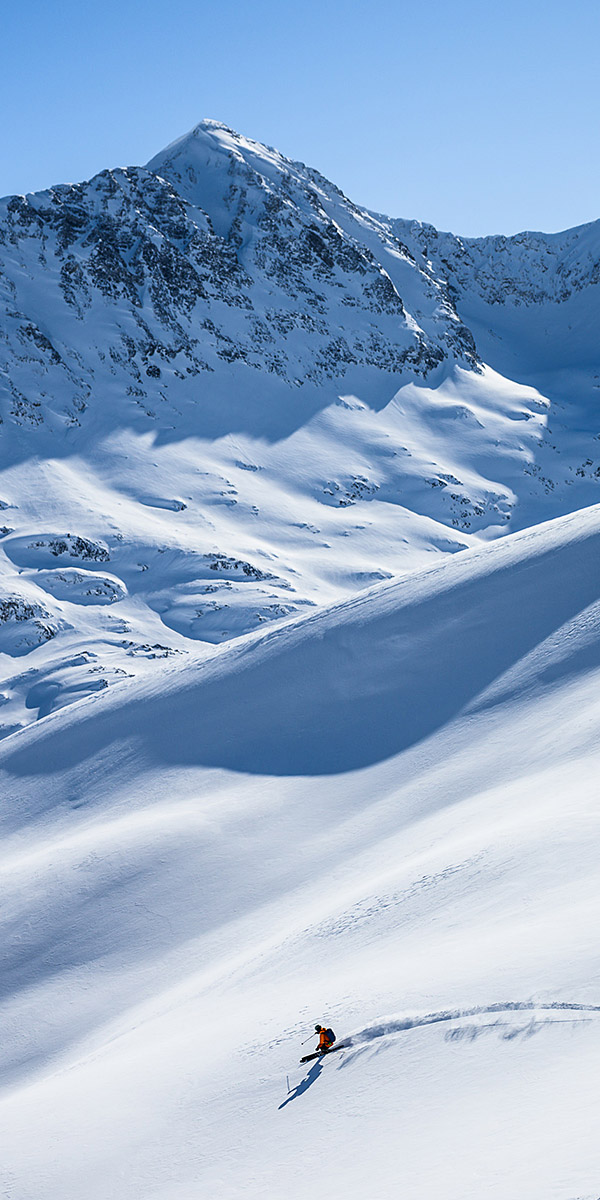 experience-inset vertical image of single skier in orange powder skiing at Gold Rush Heli-Skiing
