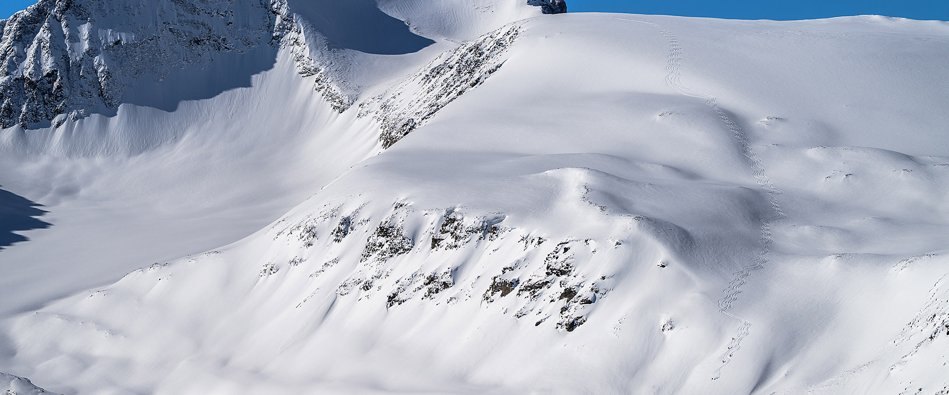 what-to-expect-26 photo of 5 skiers and their tracks down the side of a large mountain at Gold Rush Heli-Skiing