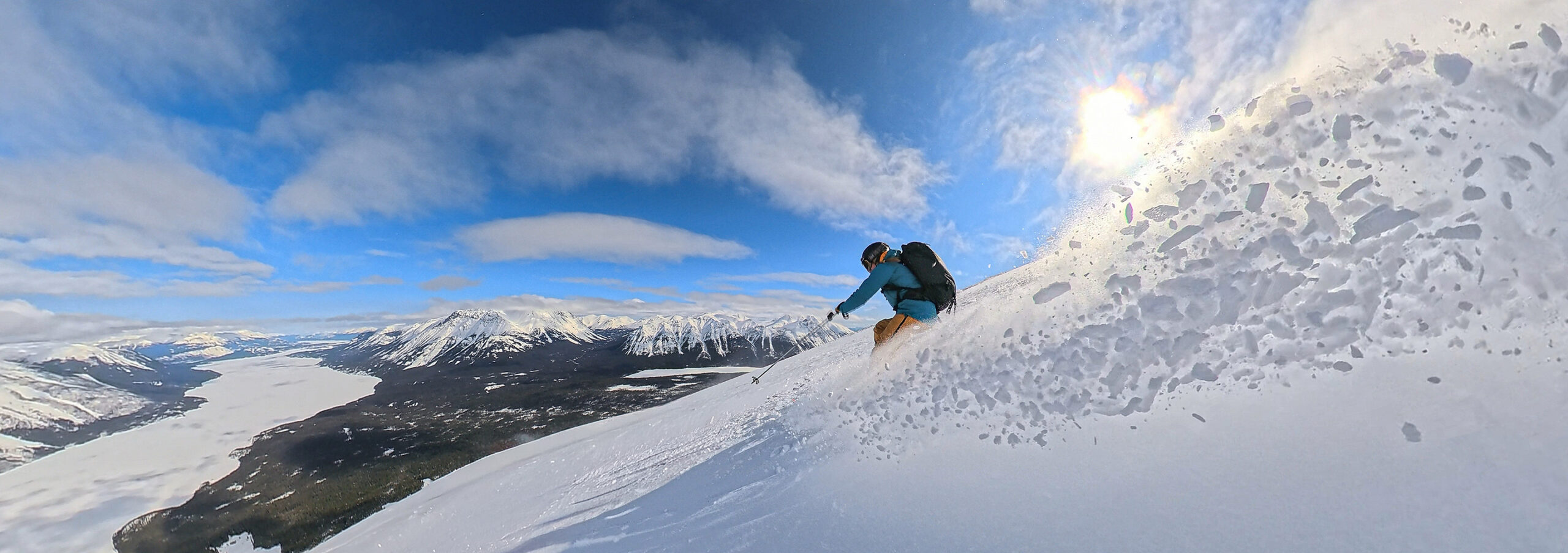 Skier in blue skis powder overlooking lake and mountains at Gold Rush Heli-Skiing